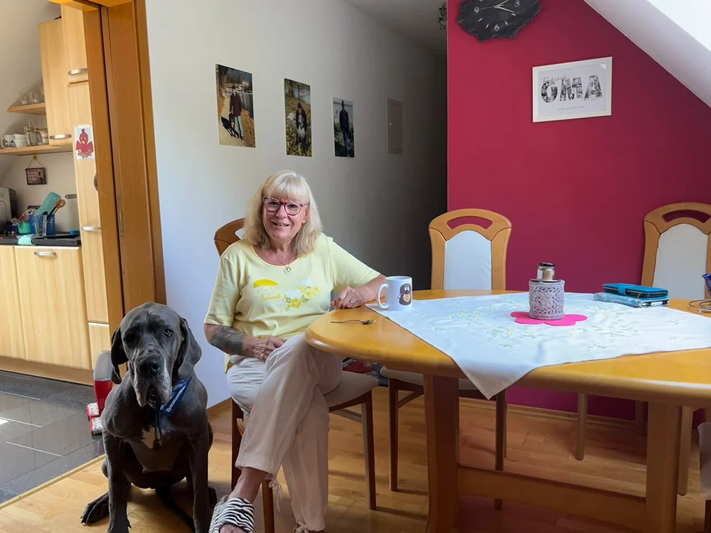 Eine Frau sitzt mit ihrer Deutschen Dogge am Tisch während sie ihre gemeinsame Geschichte erzählt